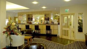A hotel lobby with a reception desk, seating area, and a large decorative plant. - The Gower Golf Club (Swansea)