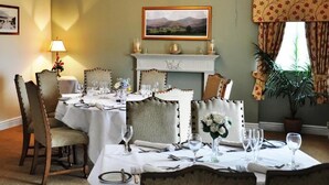 A dining room with a fireplace, a chandelier, and a framed landscape painting on the wall. - The Gower Golf Club (Swansea)