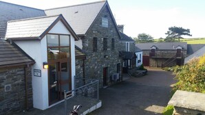 A reception area with a sign, a stone building with a sloped roof, and a pathway leading to a gate. - The Gower Golf Club (Swansea)