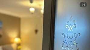 A hotel room with a bed, a nightstand with a lamp, and a decorative glass panel with etched designs. - The Gower Golf Club (Swansea)