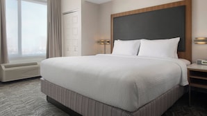 Una camera d'albergo con un letto grande, un comodino, una lampada a parete e una finestra con tende.
