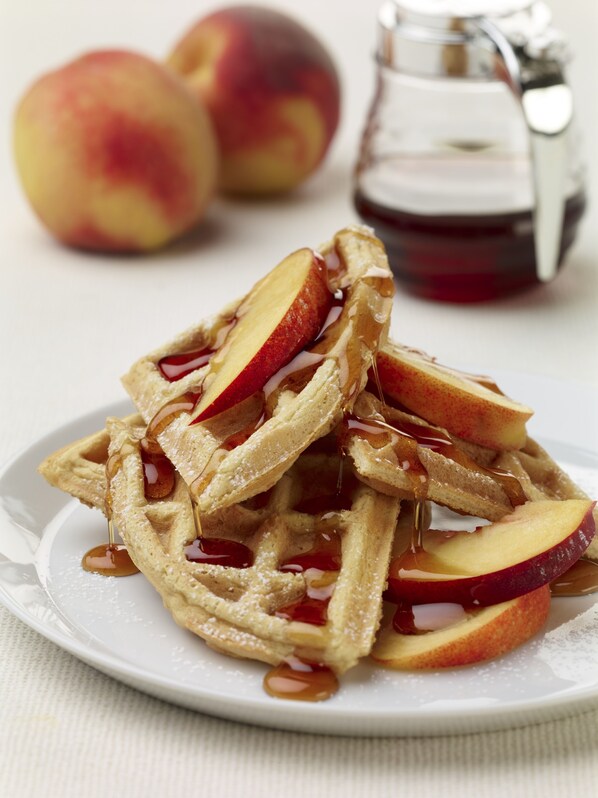 A plate of waffles with apple slices and syrup.