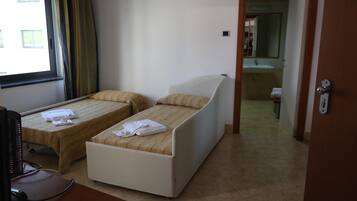 Habitación de hotel con dos camas individuales, un escritorio con una computadora, y un baño visible a través de una puerta abierta.