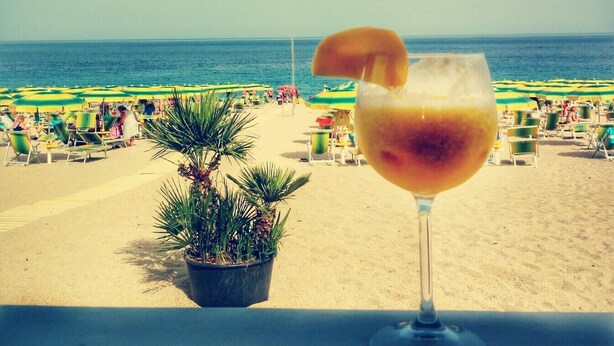 A beach view with a drink in a glass, a palm plant, and beach chairs. - Park Hotel Mirabeau (Gasperina)