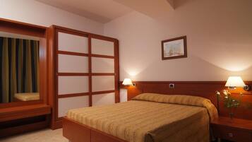 A hotel room with a bed, bedside lamps, a wooden headboard, a window with curtains, and a picture on the wall.