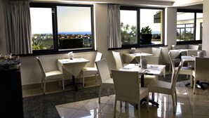 A restaurant with white wicker furniture, large windows with curtains, and a view of the city and ocean. - Park Hotel Mirabeau (Gasperina)