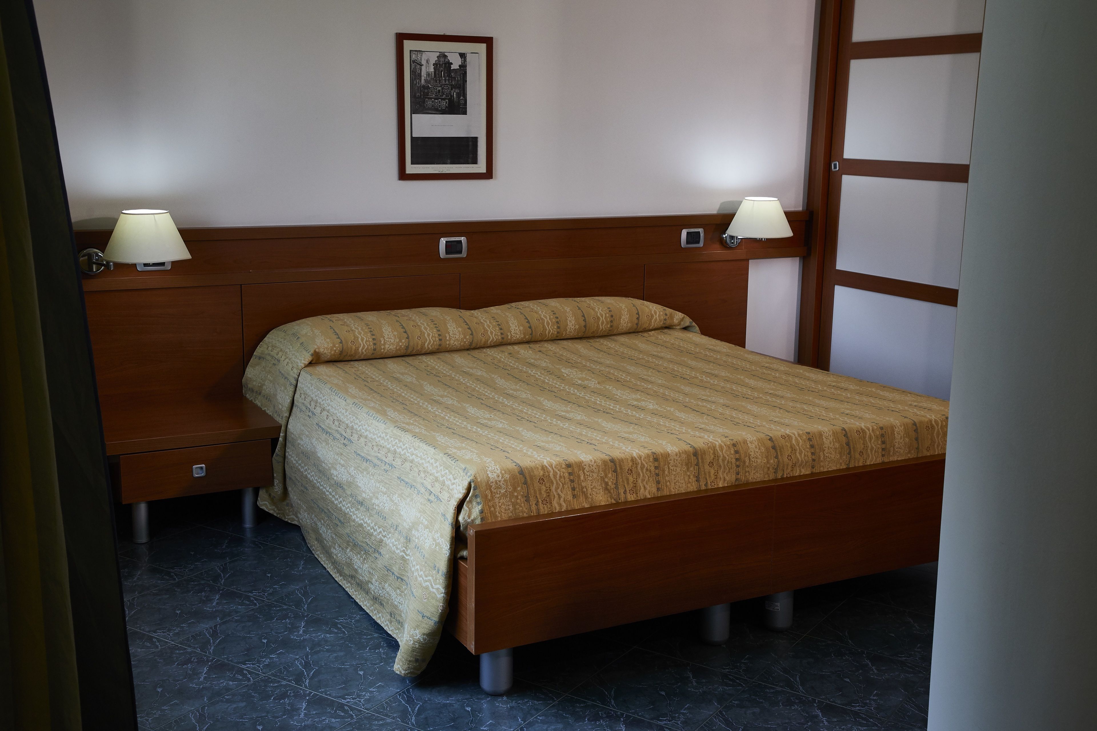 A neatly made bed with a wooden headboard and two bedside tables, each with a lamp.