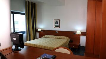 Una camera d'albergo con un letto, una scrivania, un computer, lampade e un quadro appeso al muro.