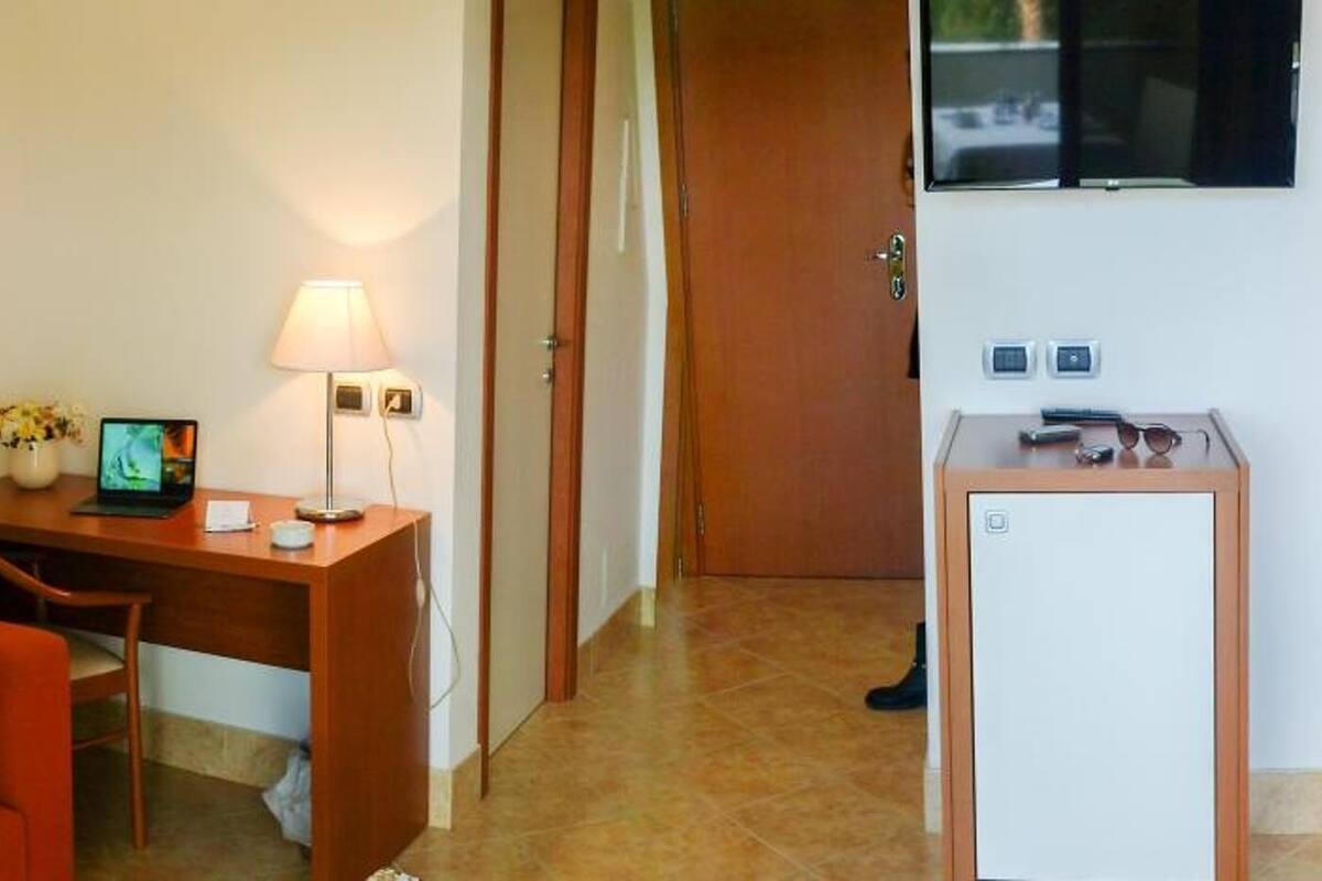 Ein Hotelzimmer mit einem Bett, einem Schreibtisch mit Lampe, einem kleinen Tisch mit Fernseher und einer Tür.