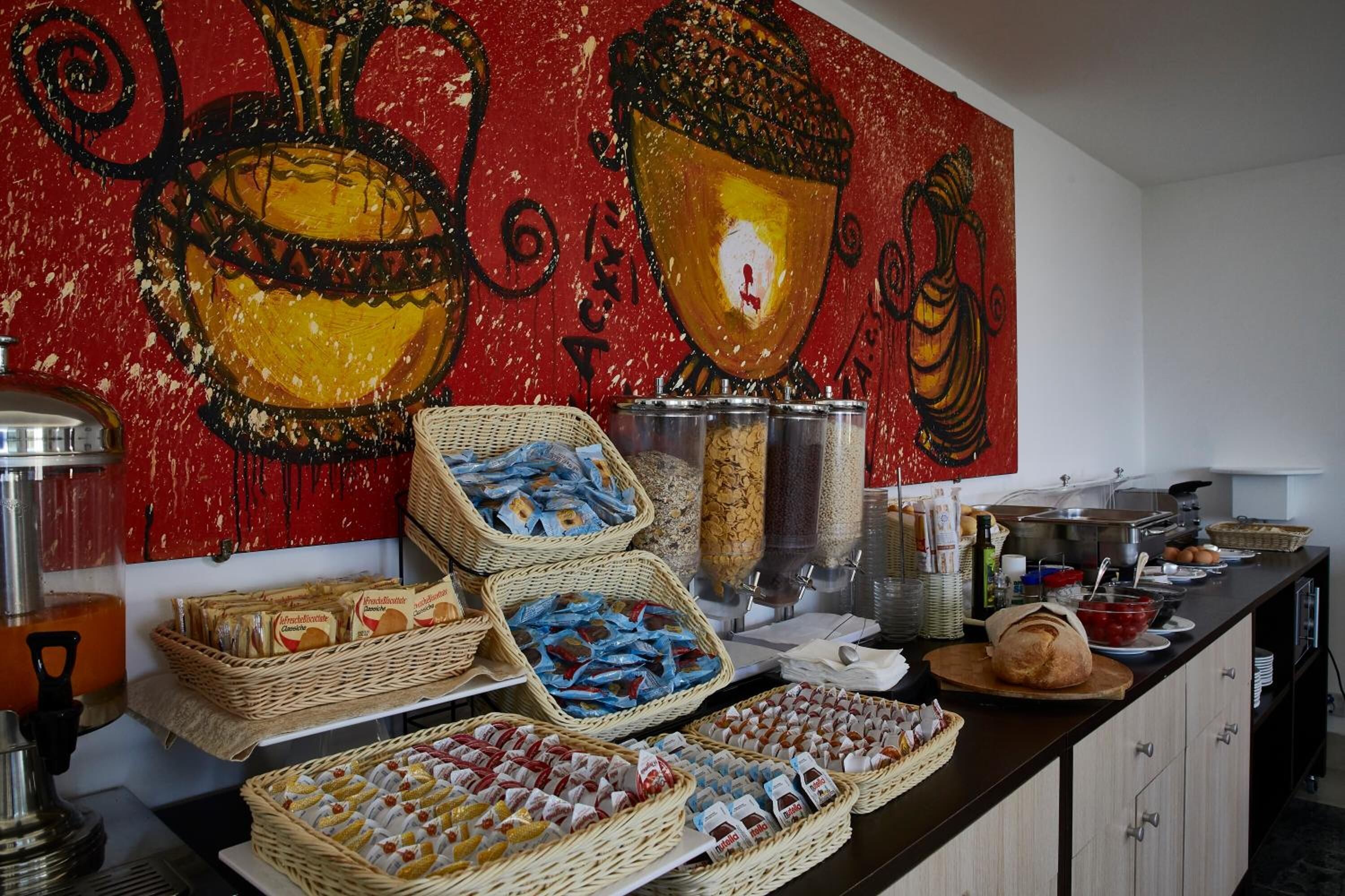 Montaje de bufé con diferentes platillos y cestas, una máquina de café y un cuadro decorativo grande en la pared.