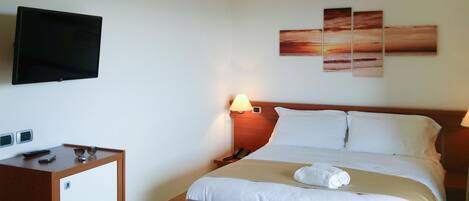 A hotel room with a bed, bedside table, lamp, TV, and artwork on the wall.