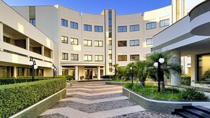 A modern multi-story hotel with a central courtyard, featuring a geometric tile pattern, and surrounded by greenery and plants. - Park Hotel Mirabeau (Gasperina)
