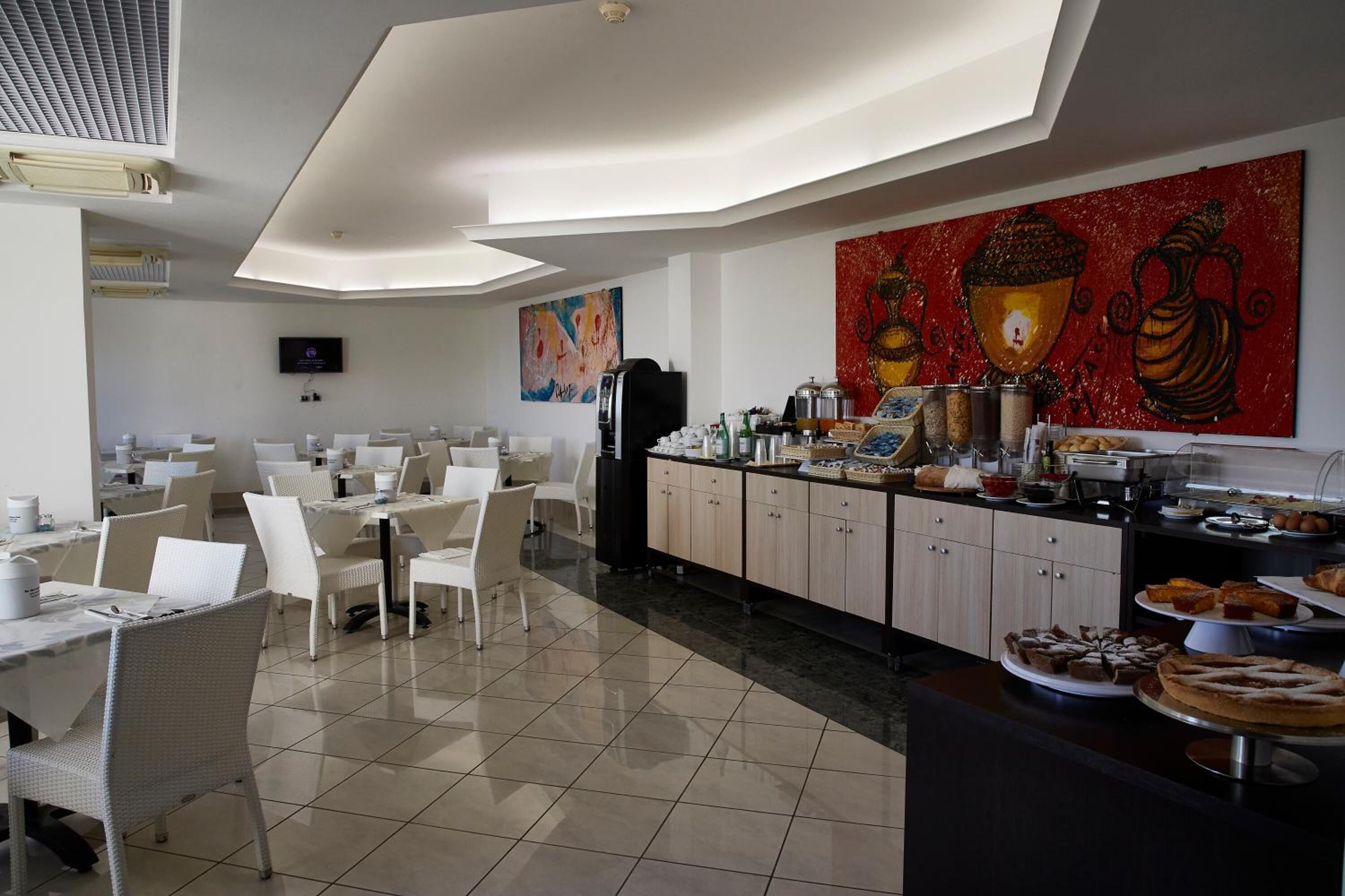 A modern dining area with white furniture, a buffet counter with various food items, and a large abstract painting on the wall.