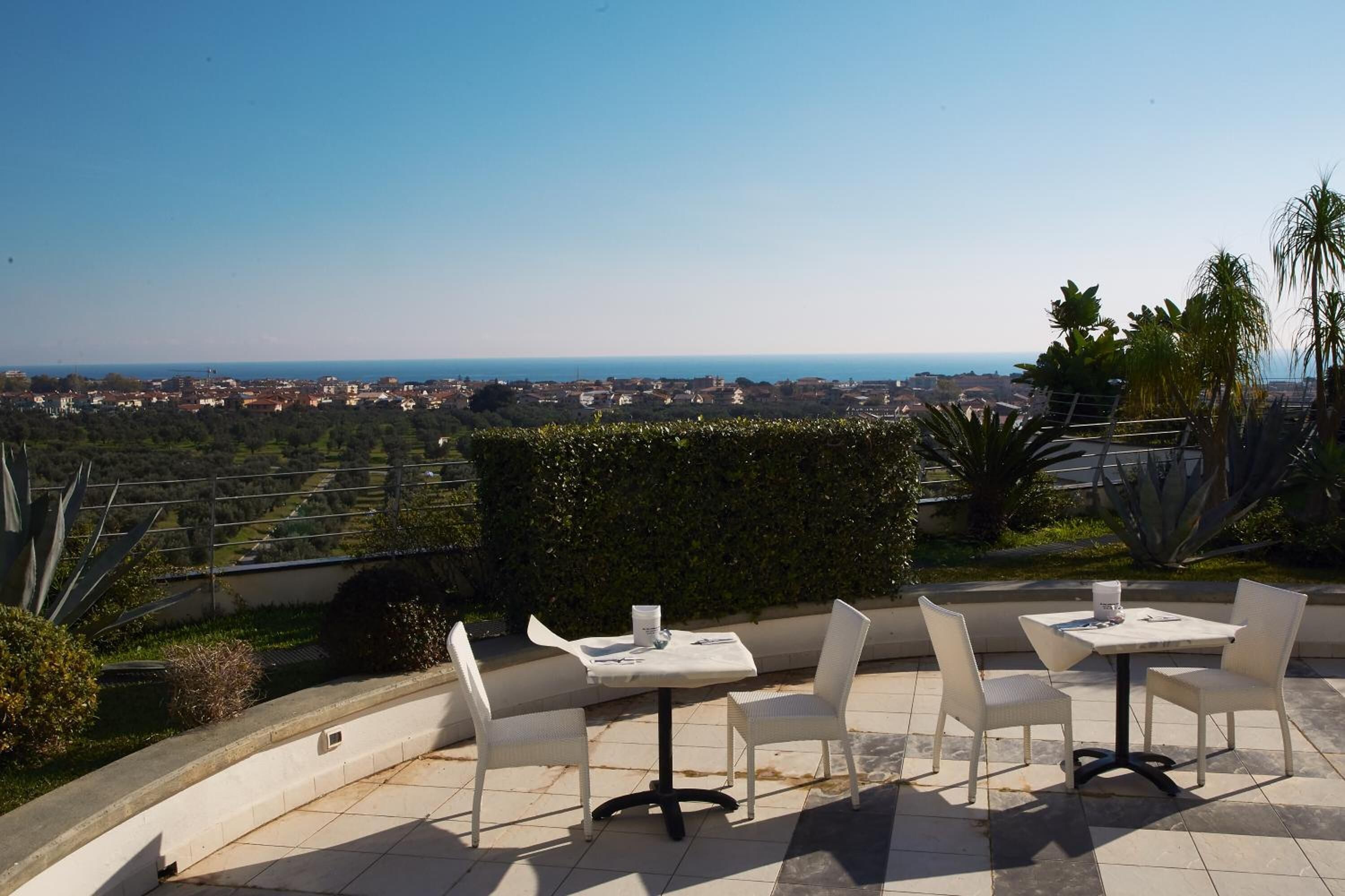 A terrace with two tables and chairs, overlooking a coastal cityscape.