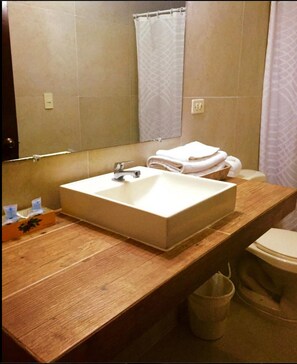 Een badkamer met een houten wastafelmeubel, een witte wastafel, een spiegel, een handdoekhouder en een toilet.
