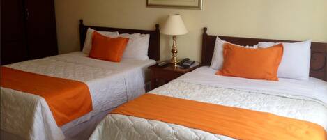 Two twin beds with white and orange bedding, a bedside table with a lamp, and a framed picture on the wall.