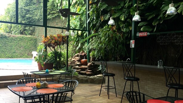 An indoor patio area with tables and chairs, a pool, and lush greenery. - Hotel Alicante San Salvador (Antiguo Cuscatlán)