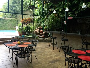 Een binnenterras met tafels, stoelen, een zwembad en weelderige beplanting.