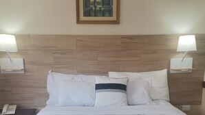 A hotel room with a large bed, white bedding, a wooden headboard, two bedside lamps, a nightstand with a phone, and a framed picture on the wall. - Hotel Alicante San Salvador (Antiguo Cuscatlán)