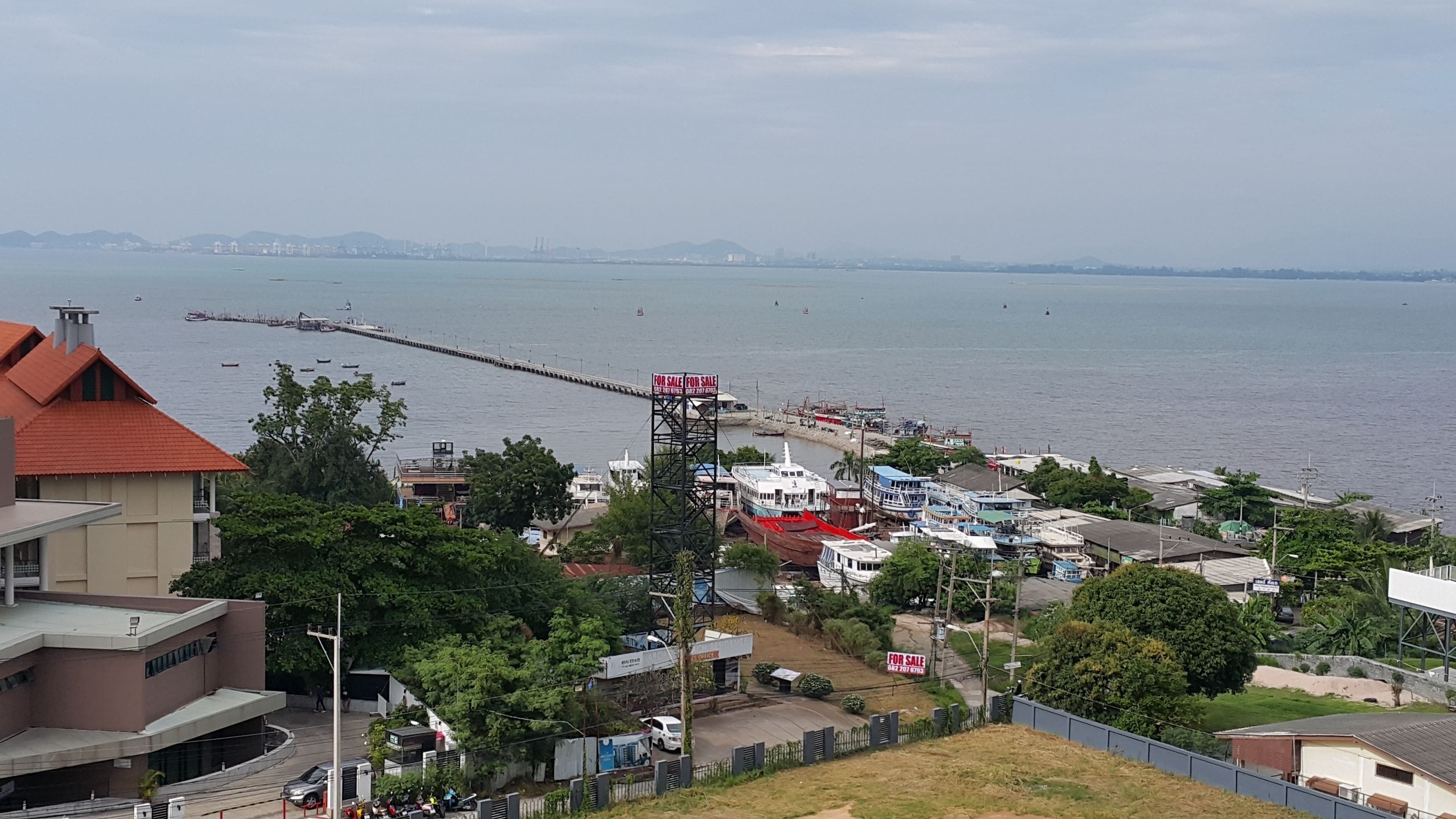 A coastal town with a pier extending into the water, surrounded by residential buildings and greenery.