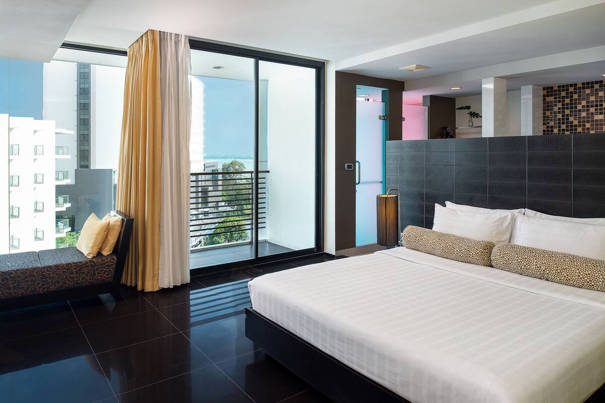 Quarto de hotel moderno com uma cama grande, um sofá e uma varanda com vista para a cidade.