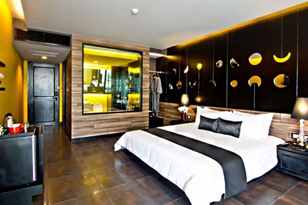 Quarto de hotel moderno com uma cama grande, televisão e vista para a cidade através de uma janela ampla.