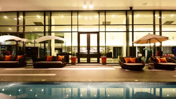 A poolside area with seating and umbrellas, a glass facade, and a reception desk. - Tsix5 Hotel (Pattaya)