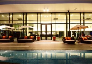 A poolside area with seating and umbrellas, a glass facade, and a reception desk. - Tsix5 Hotel (Pattaya)