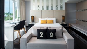 A modern hotel room with a large bed, two bedside tables, a desk, and a sofa with numbered cushions. - Tsix5 Hotel (Pattaya)