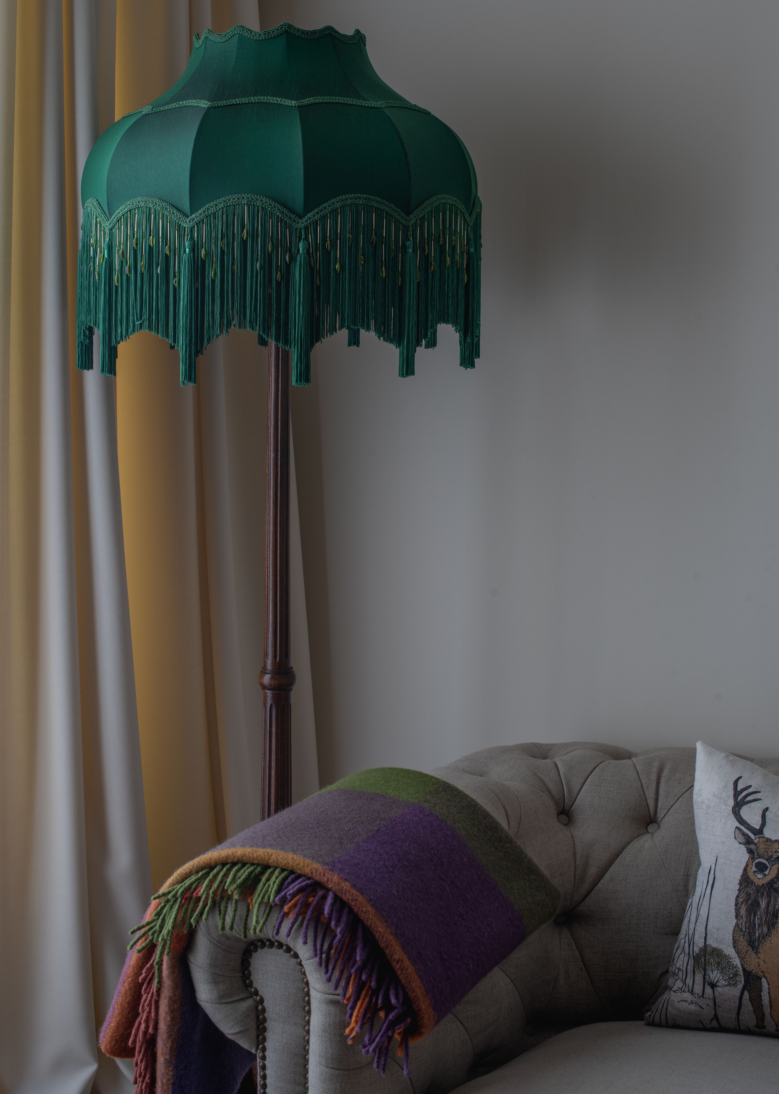 A room with a tufted sofa, a patterned throw blanket, and a green fringed floor lamp.