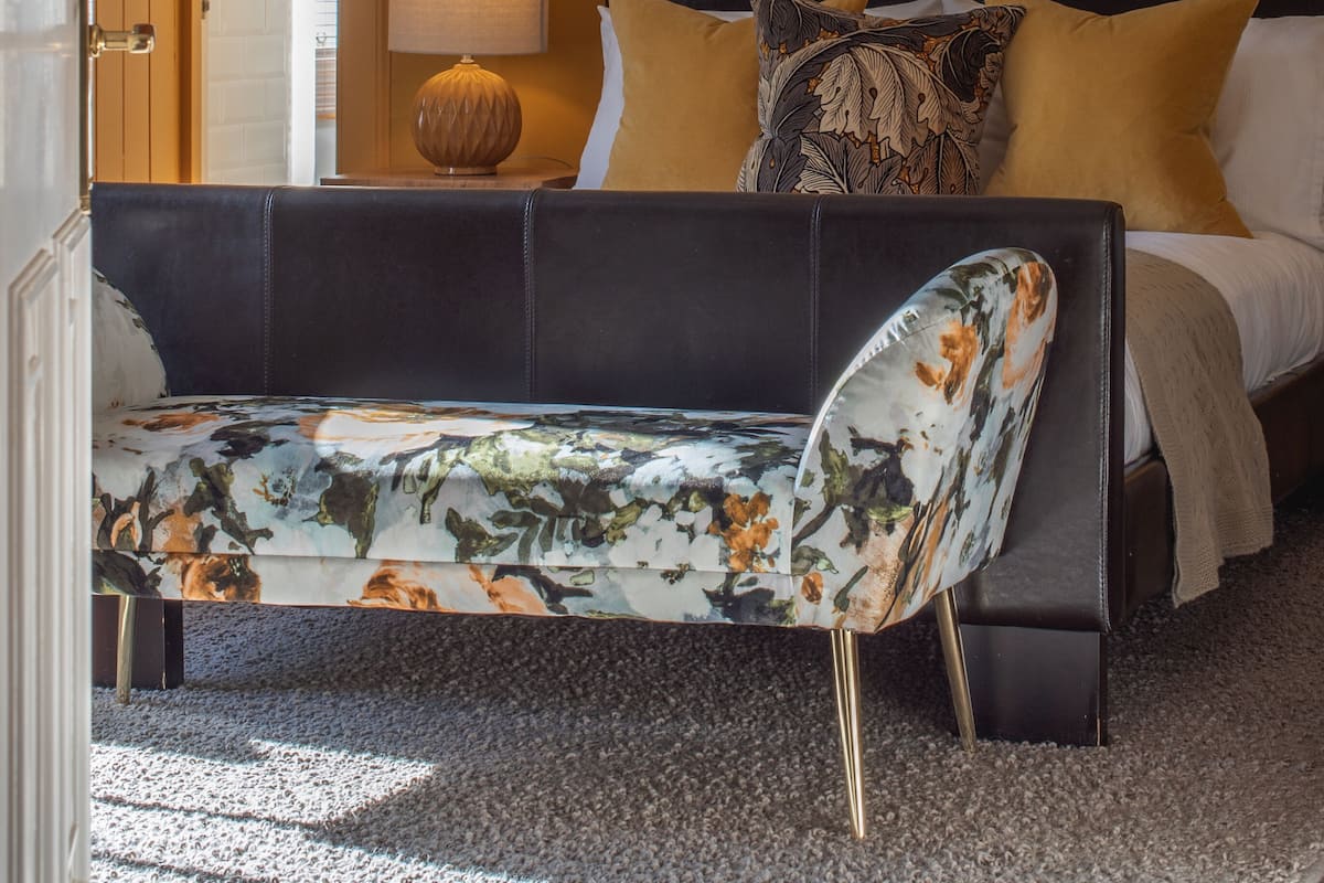 A hotel room with a bed, a sofa, a lamp, and a framed artwork on the wall.