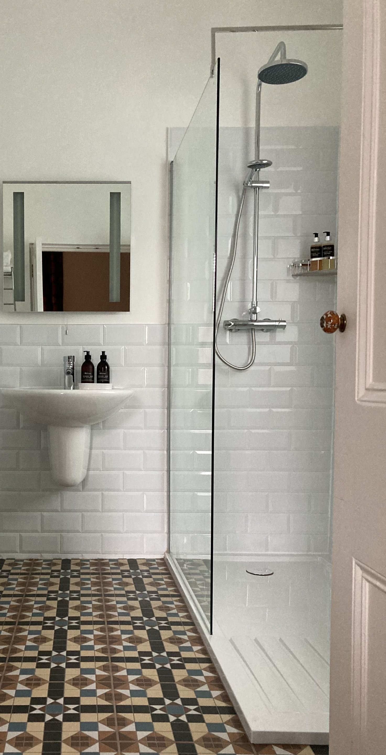 A bathroom with a white sink, mirror, shower, and patterned floor tiles.