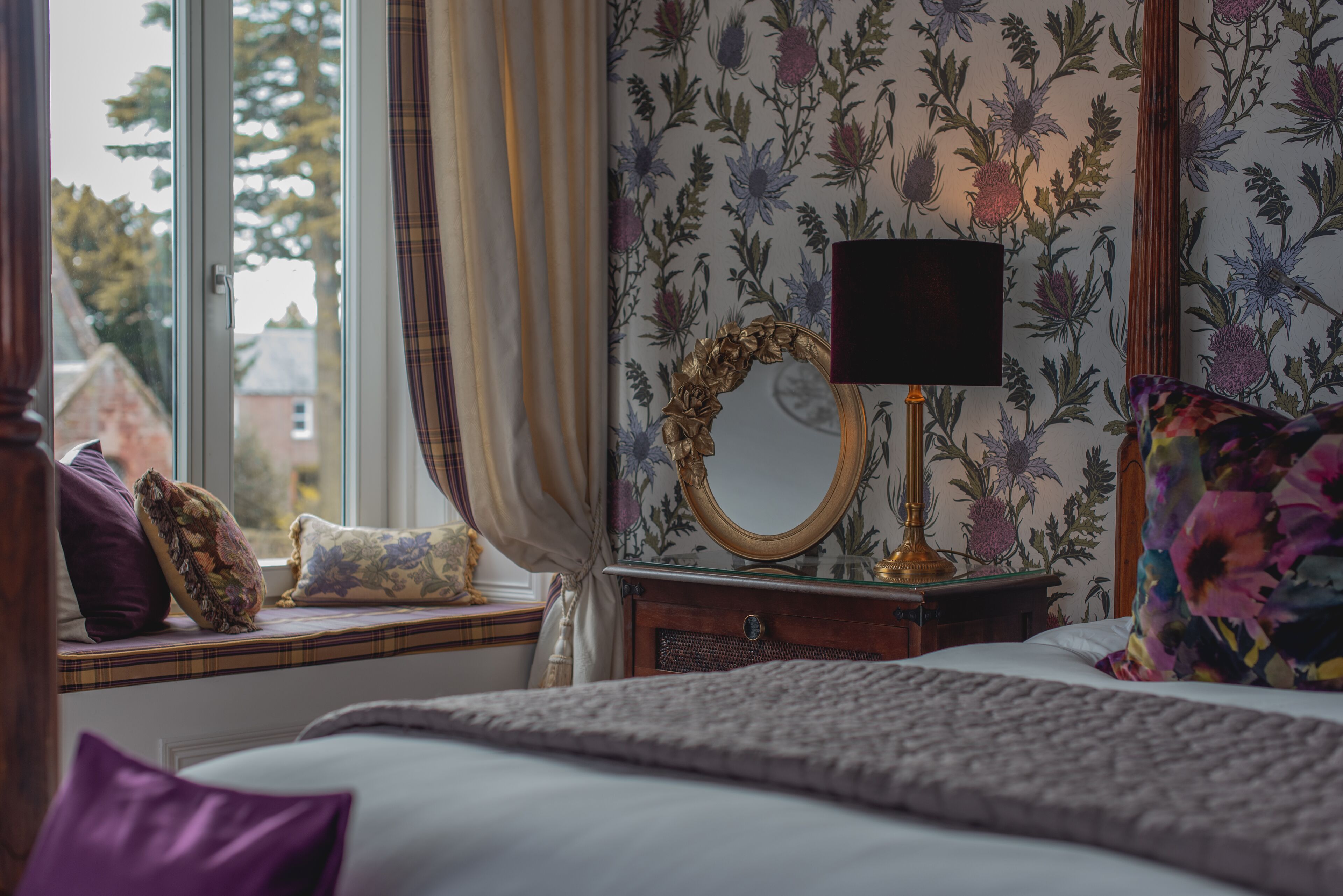 A bedroom with a window seat, a mirror, and a bedside table.