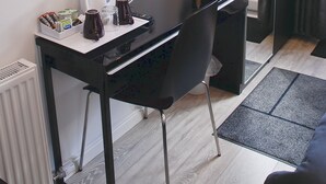 Een moderne kamer met een zwart bureau, een wandgemonteerde televisie, een spiegel en een raam met gordijnen.