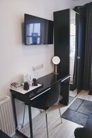 Quarto moderno com escrivaninha preta, televisão montada na parede, espelho e janela com cortinas.