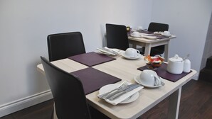 Een eettafel gedekt met borden, bestek en een theepot, omringd door stoelen.