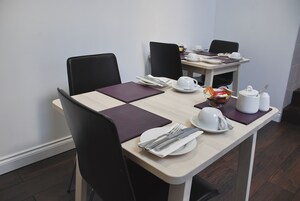 Mesa de jantar posta com pratos, talheres e um bule, com cadeiras ao redor.