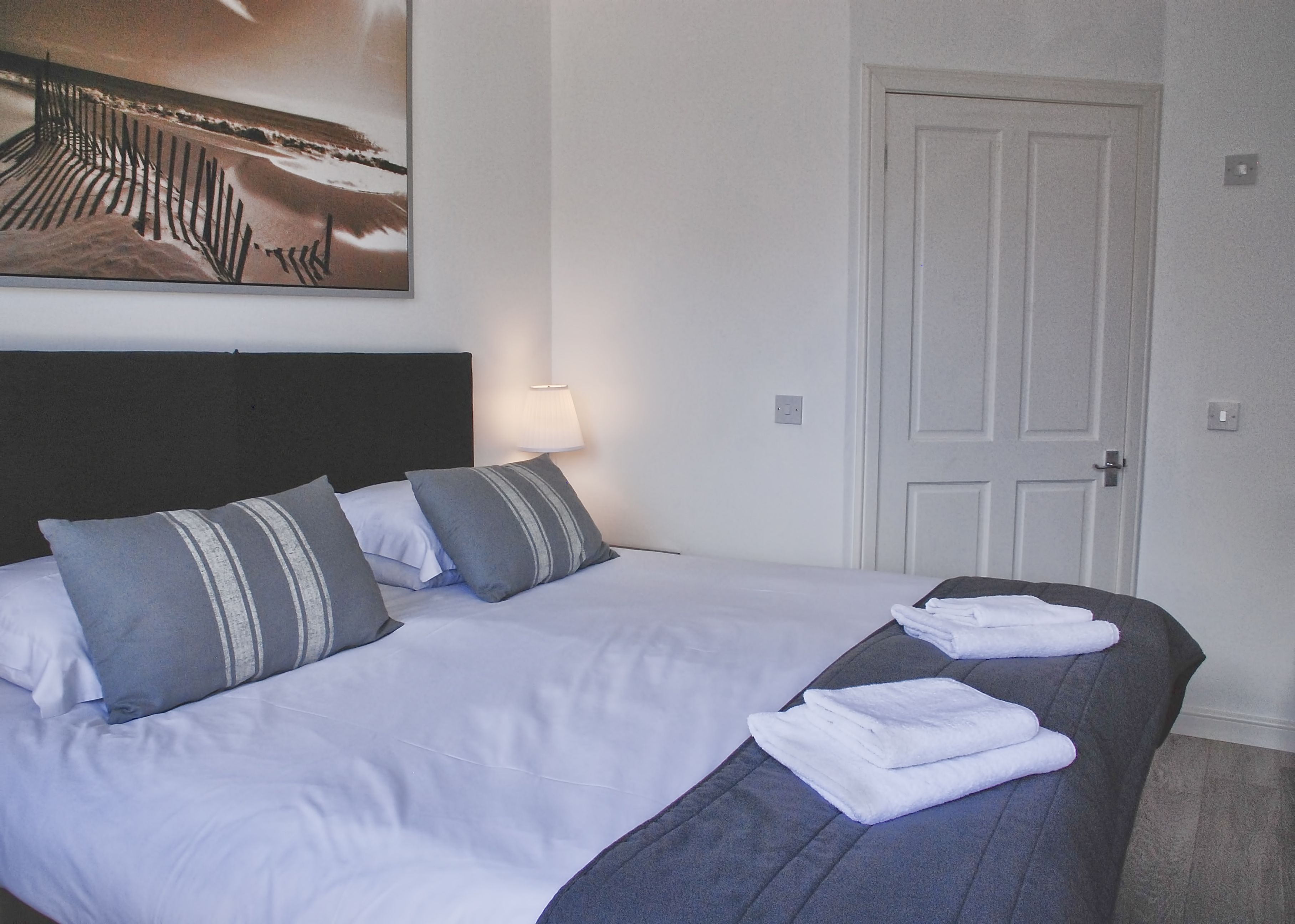 A neatly made bed with white and gray bedding, a dark headboard, and a framed picture above it.