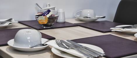 Una mesa de comedor ordenada con platos, cubiertos y un tazón de cereales.