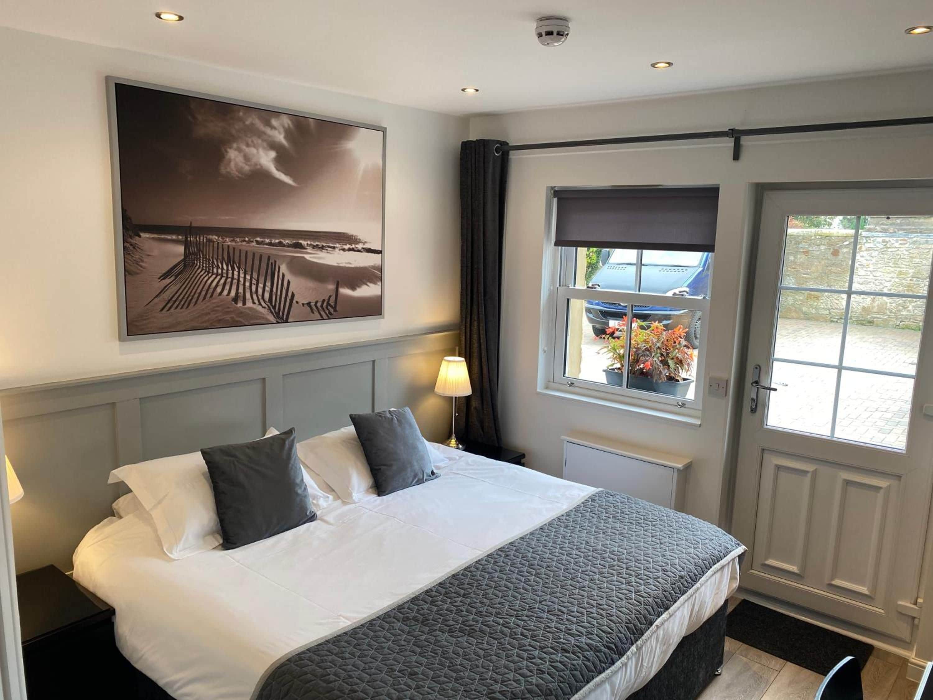 A hotel room with a bed, a window with a view of the outside, a wall-mounted picture, and a door with a window.