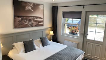 A hotel room with a bed, a window with a view of the outside, a wall-mounted picture, and a door with a window.