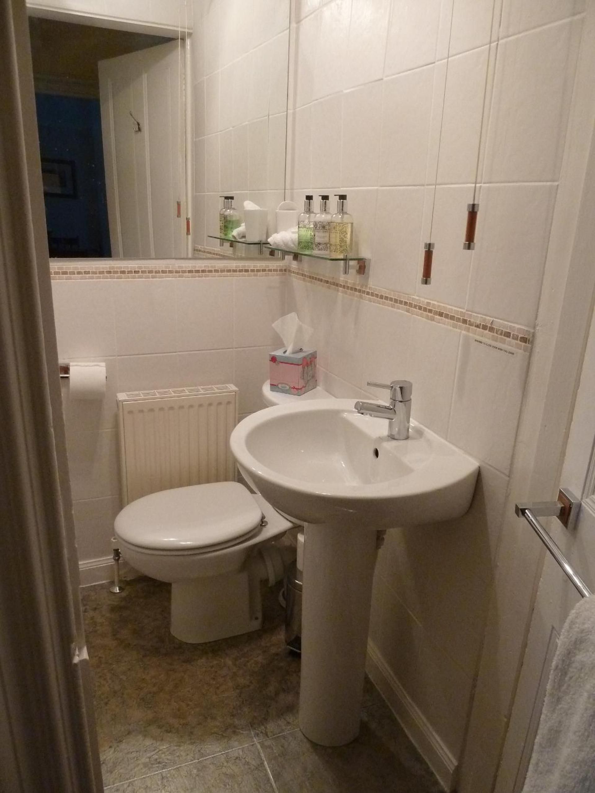 A bathroom with a toilet, a sink, and a mirror. There is a towel rack above the sink and a toilet paper holder on the wall.
