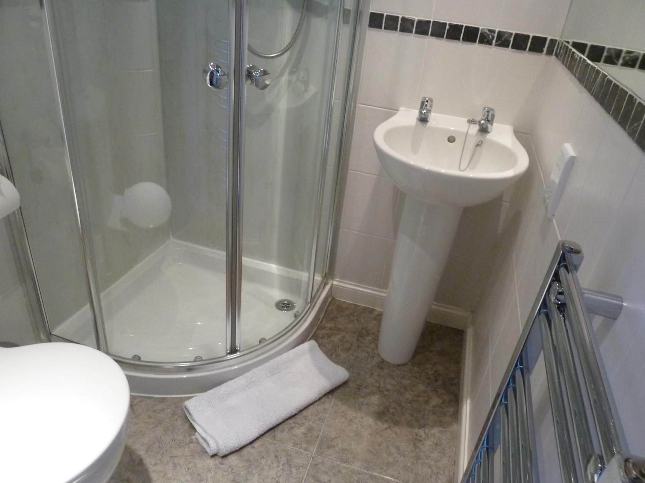 Et badeværelse med en glasafskærmet bruseniche, en hvid vask og et toilet.