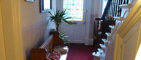 A hallway with a wooden bench, a potted plant, a red carpet, a staircase with white railings, and a door with a stained glass window.