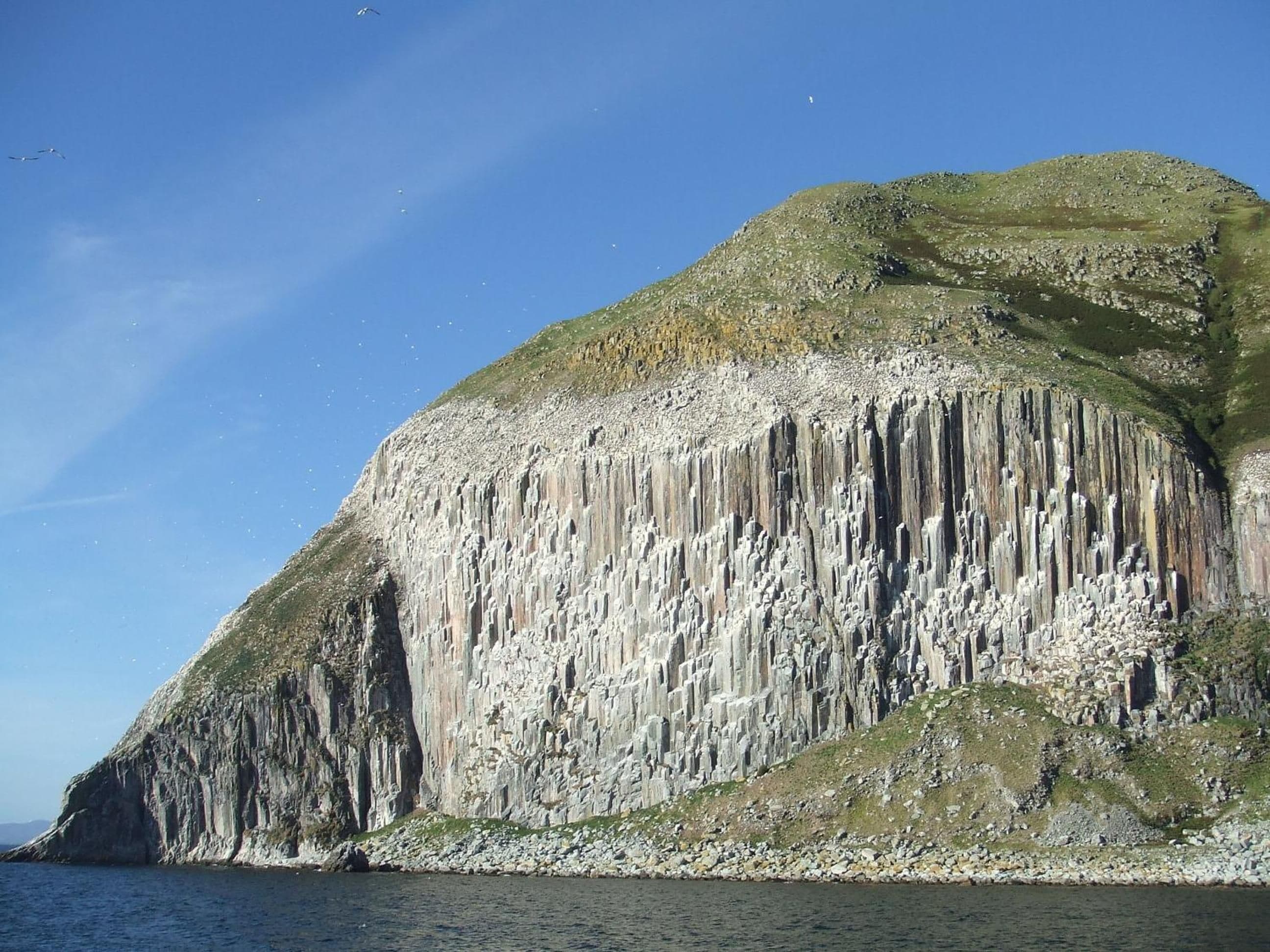 Une falaise côtière avec des formations rocheuses verticales et un ciel dégagé.