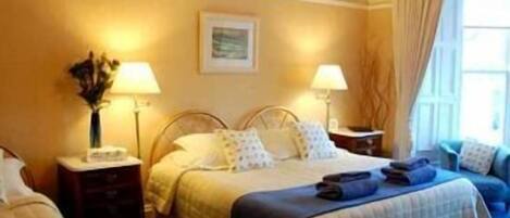 A hotel room with a bed, bedside tables, lamps, a vase with flowers, and a window with curtains.