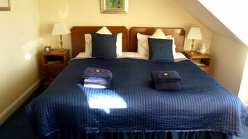 Una cama bien hecha con colcha y almohadas azules, dos mesitas de noche con lámparas y un cuadro en la pared.