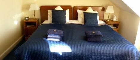 A neatly made bed with a blue quilt and pillows, two bedside tables with lamps, and a framed picture on the wall.
