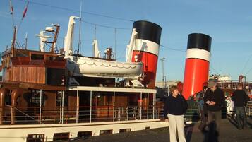 Een groot schip met twee hoge schoorstenen, een houten dek en een menigte mensen.