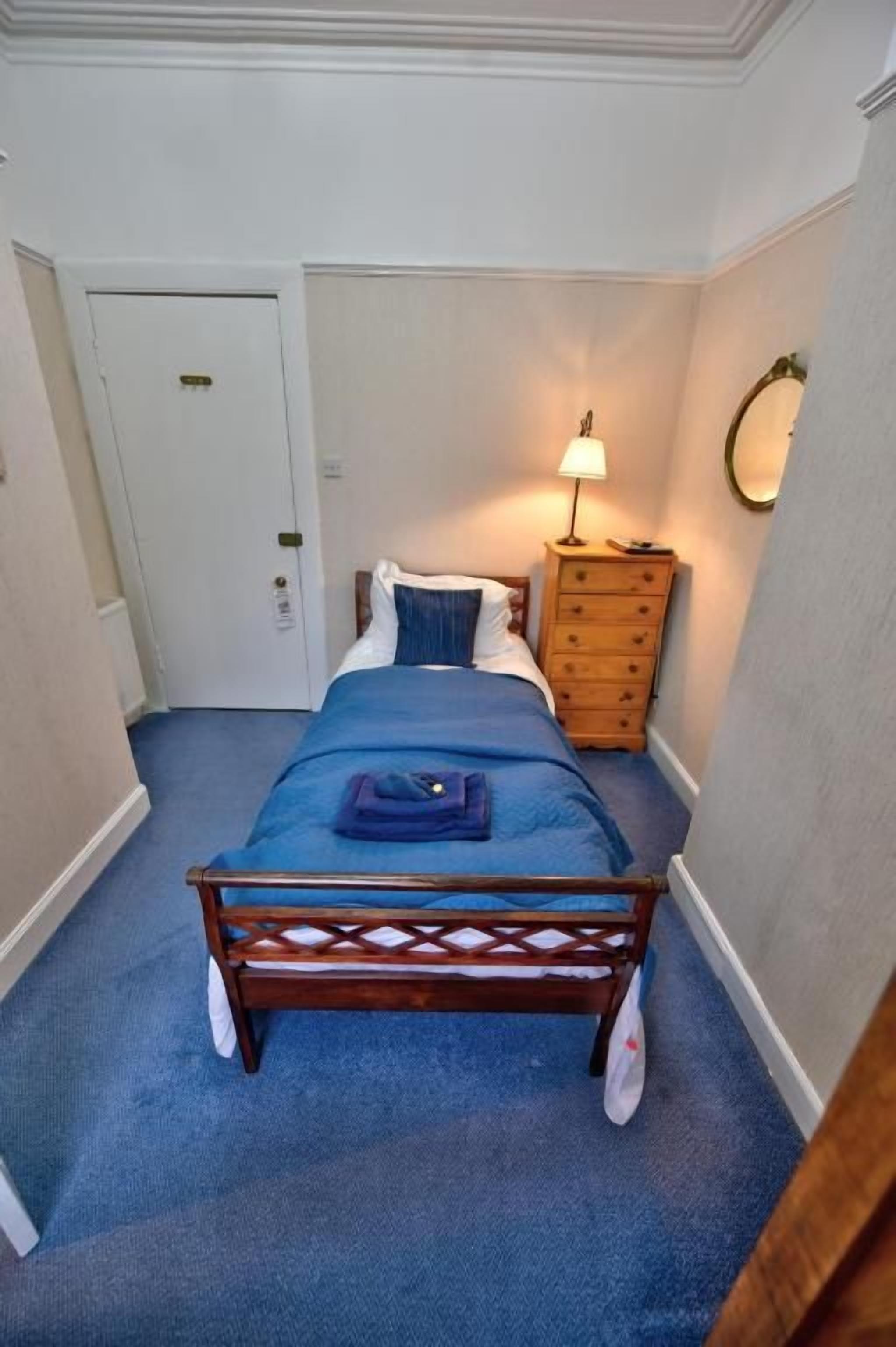 A bedroom with a wooden bed, a dresser, a nightstand, and a wall-mounted lamp.